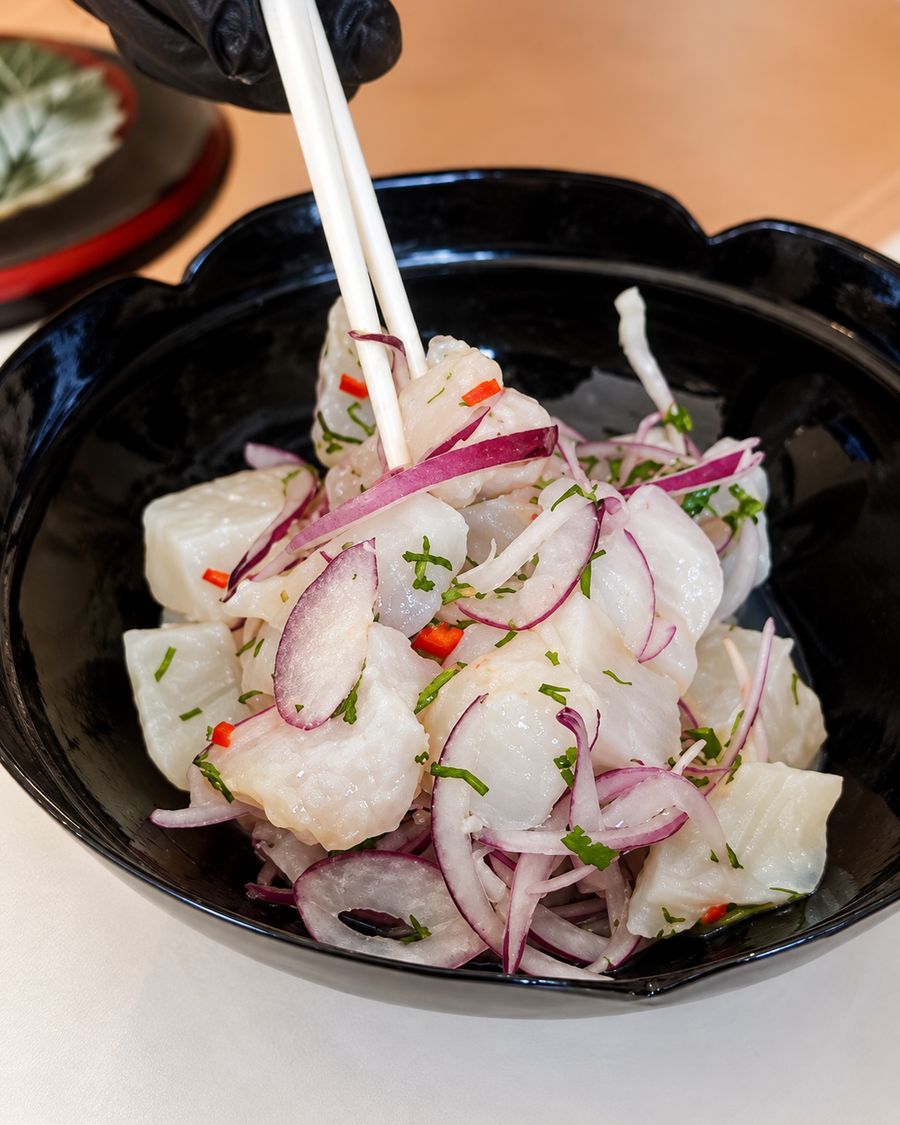 Ceviche con pescado blanco, cebolla morada y ají, servido en un bol negro.