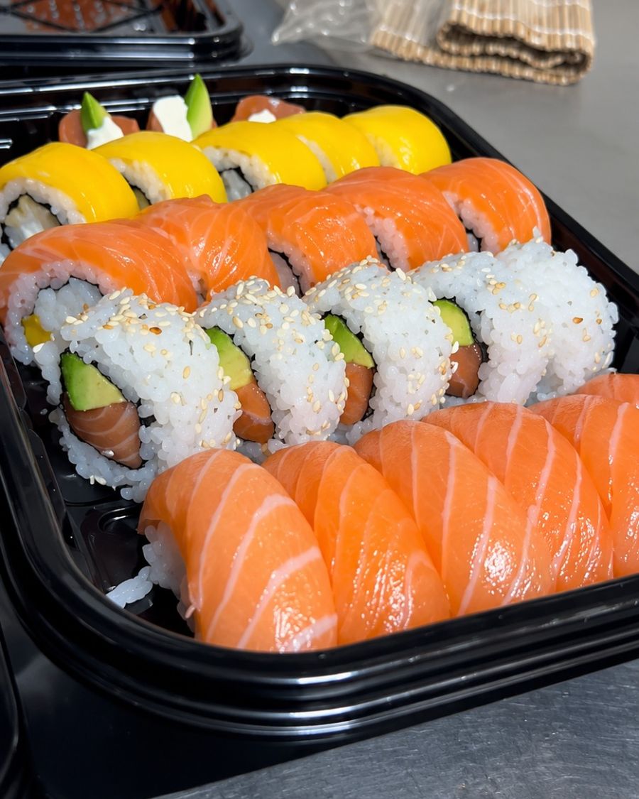 Pedido armado en bandejas negras, con rolls de salmón, palta y mango, listo para salir.