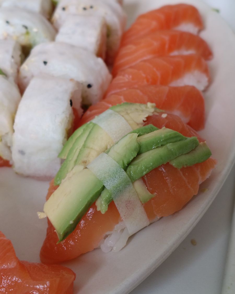 Nigiris de salmón con láminas de palta, junto a rolls, en un plato blanco.